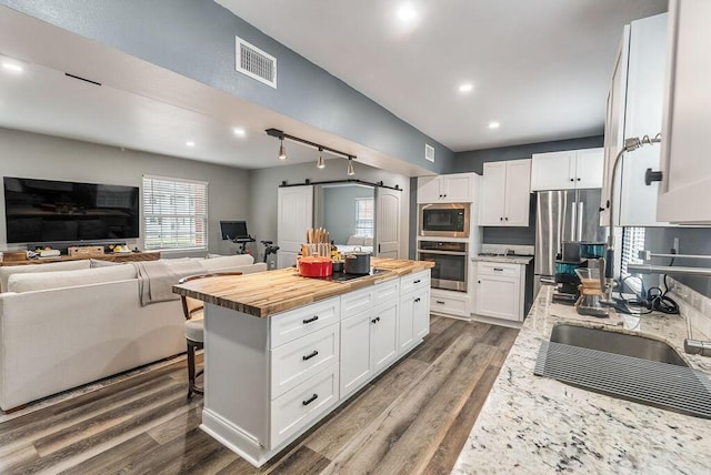 kitchen with appliances with stainless steel finishes, a kitchen breakfast bar, butcher block countertops, a barn door, and white cabinetry