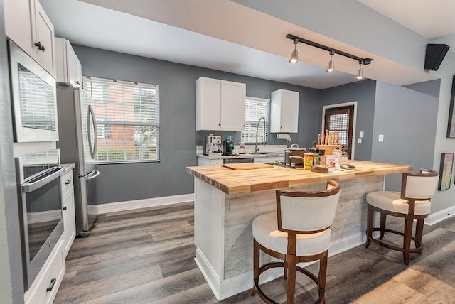 kitchen featuring wooden counters, stainless steel appliances, white cabinets, a breakfast bar, and hardwood / wood-style floors