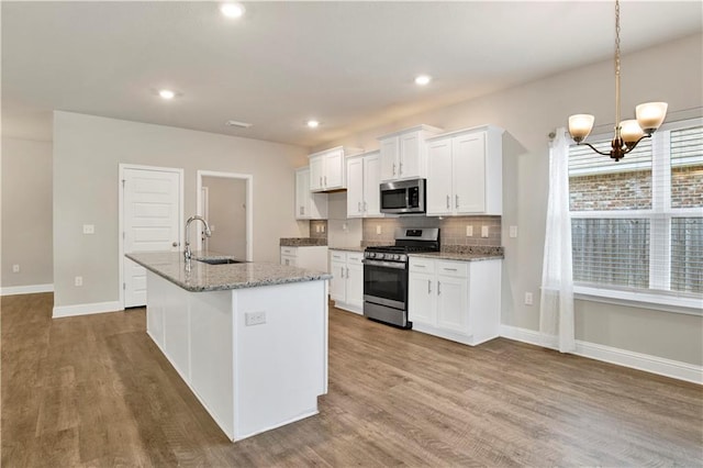 kitchen with a kitchen island with sink, sink, appliances with stainless steel finishes, a notable chandelier, and white cabinetry