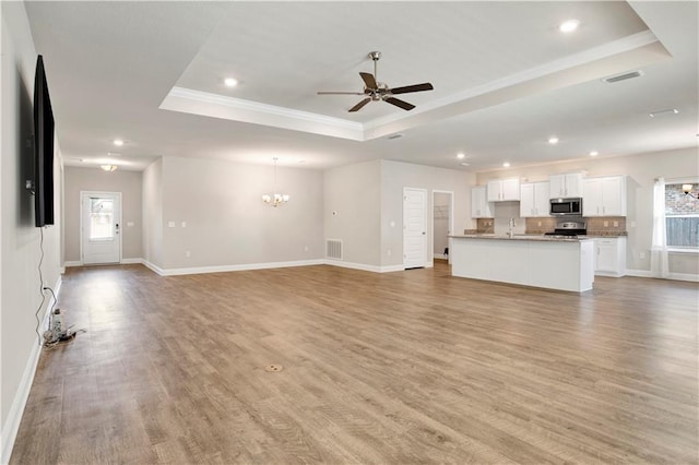 unfurnished living room with light hardwood / wood-style floors, a wealth of natural light, and a tray ceiling