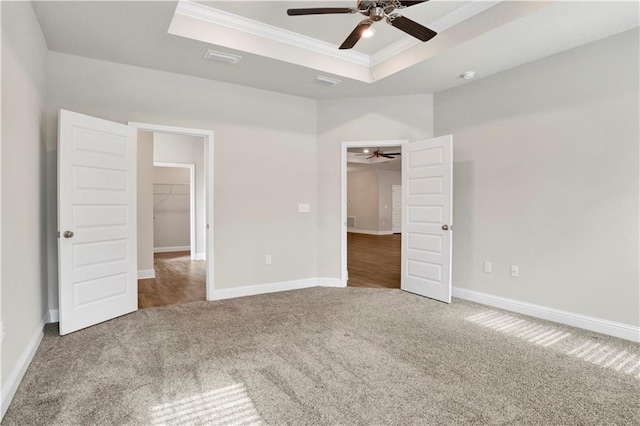 unfurnished bedroom with a raised ceiling, ceiling fan, a closet, and a spacious closet