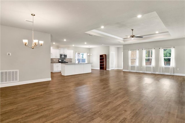 unfurnished living room featuring ceiling fan with notable chandelier, dark hardwood / wood-style floors, and a raised ceiling