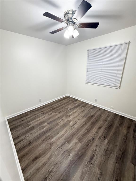 spare room with dark wood-type flooring, a ceiling fan, and baseboards