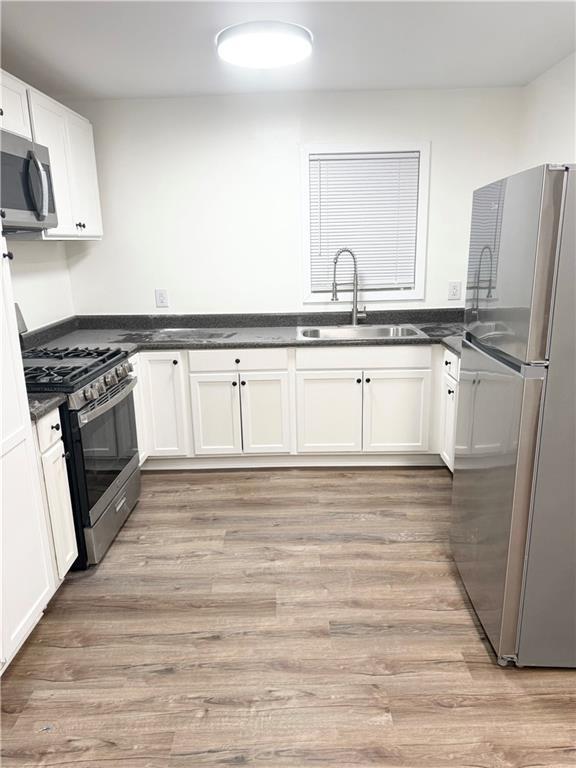 kitchen with dark countertops, a sink, light wood-style flooring, stainless steel appliances, and white cabinetry