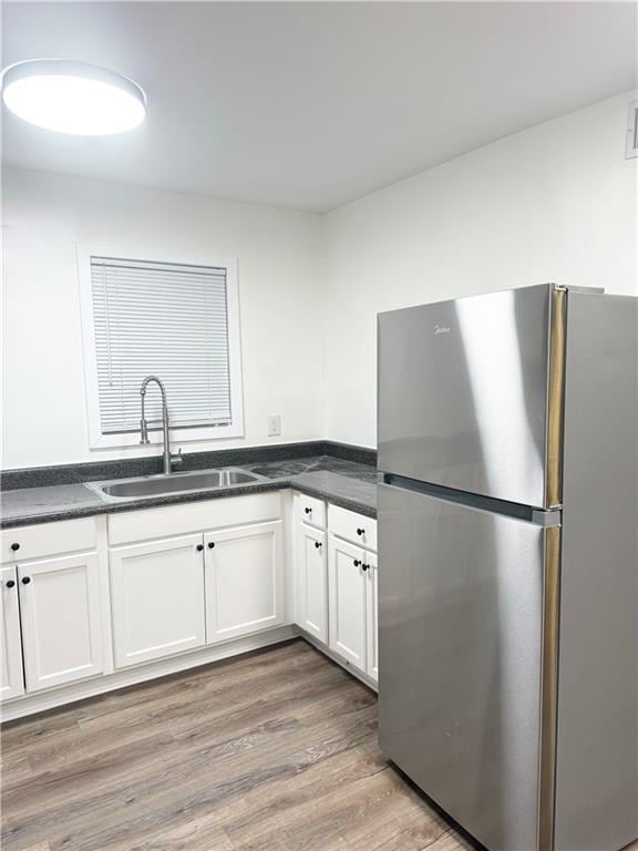kitchen featuring freestanding refrigerator, dark countertops, a sink, and wood finished floors