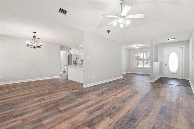 unfurnished living room with ceiling fan with notable chandelier, dark wood-style floors, visible vents, and baseboards