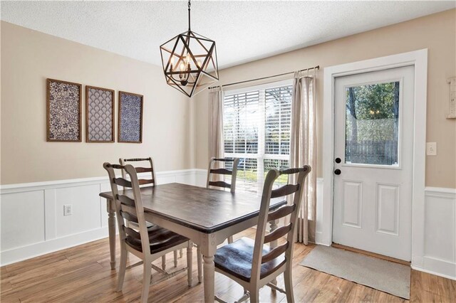 dining area featuring a textured ceiling, wainscoting, light wood-style flooring, and an inviting chandelier