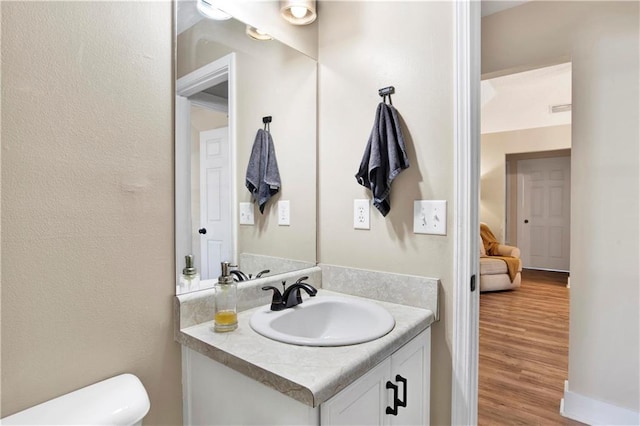 half bathroom with toilet, wood finished floors, and vanity