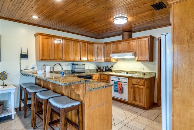 2012 Bienville Blvd, Dauphin Island, AL 36528 - kitchen with white appliances, a peninsula, under cabinet range hood, light tile patterned floors, and a kitchen breakfast bar