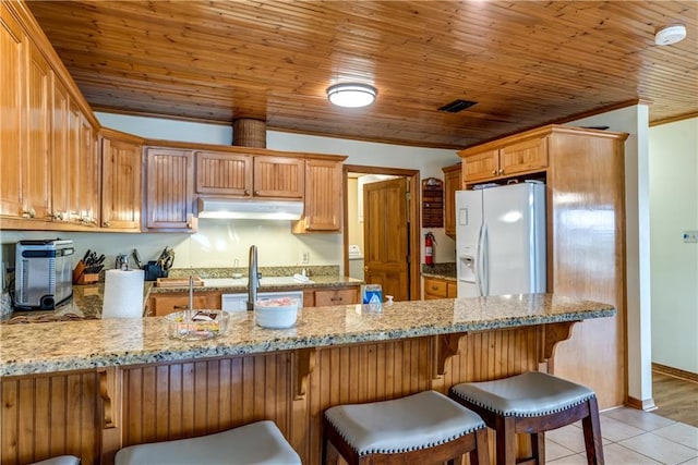 2012 Bienville Blvd, Dauphin Island, AL 36528 - kitchen with white fridge with ice dispenser, under cabinet range hood, crown molding, a peninsula, and light stone counters