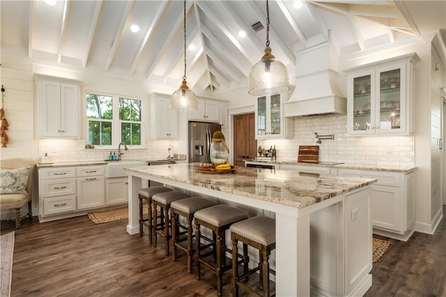 kitchen with white cabinetry, vaulted ceiling with beams, stainless steel fridge, and a kitchen island