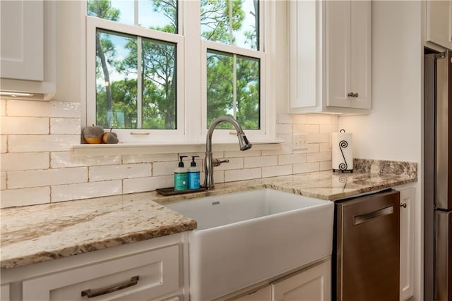 kitchen featuring a healthy amount of sunlight, decorative backsplash, appliances with stainless steel finishes, white cabinetry, and a sink