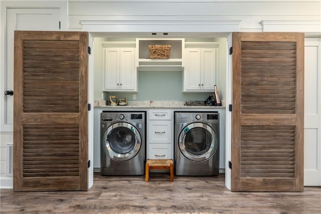 clothes washing area featuring separate washer and dryer, wood finished floors, and cabinet space