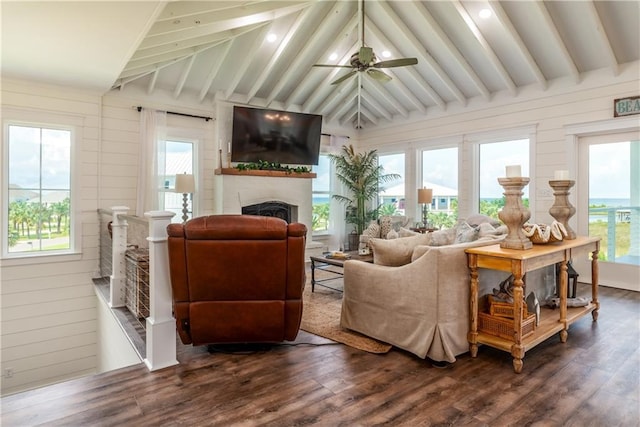 living area with dark wood-type flooring, lofted ceiling with beams, wood walls, a fireplace, and ceiling fan