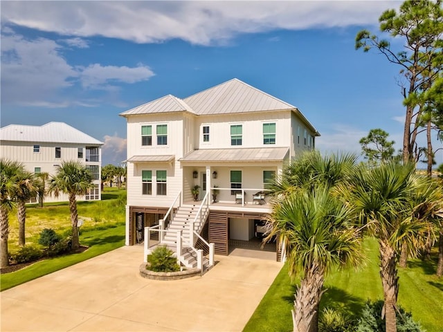 rear view of property featuring stairway, a porch, concrete driveway, a carport, and a standing seam roof