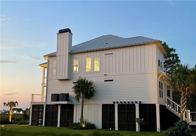 back of house at dusk featuring a lawn, board and batten siding, metal roof, and stairs