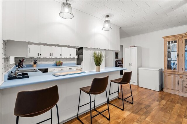 kitchen with fridge, white cabinetry, light countertops, and decorative light fixtures