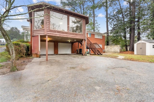 view of front of home with driveway, an outbuilding, an attached garage, stairs, and a storage unit