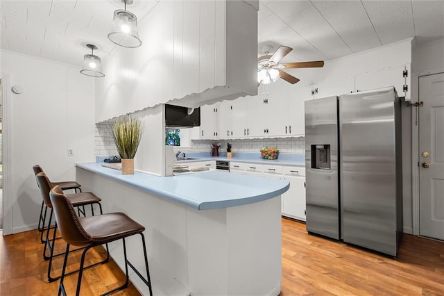 kitchen featuring light countertops, hanging light fixtures, white cabinets, stainless steel fridge, and a peninsula