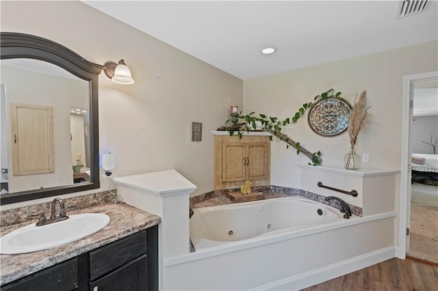 full bath with visible vents, wood finished floors, vanity, a whirlpool tub, and ensuite bath