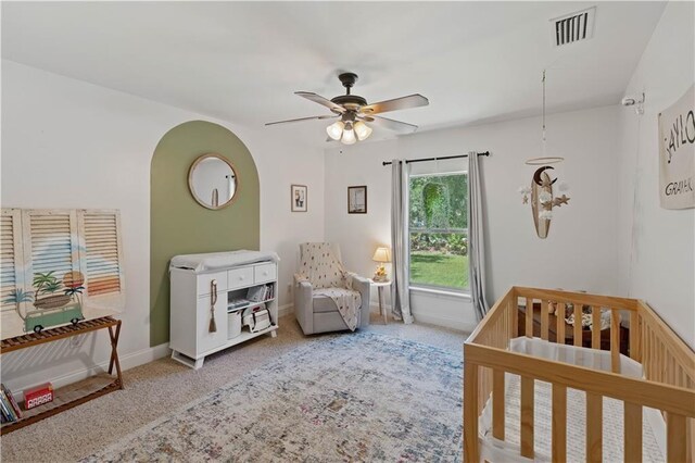 carpeted bedroom with visible vents, baseboards, ceiling fan, and a nursery area