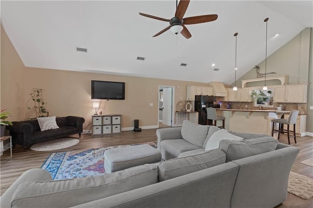 living area with high vaulted ceiling, ceiling fan, light wood-type flooring, and visible vents