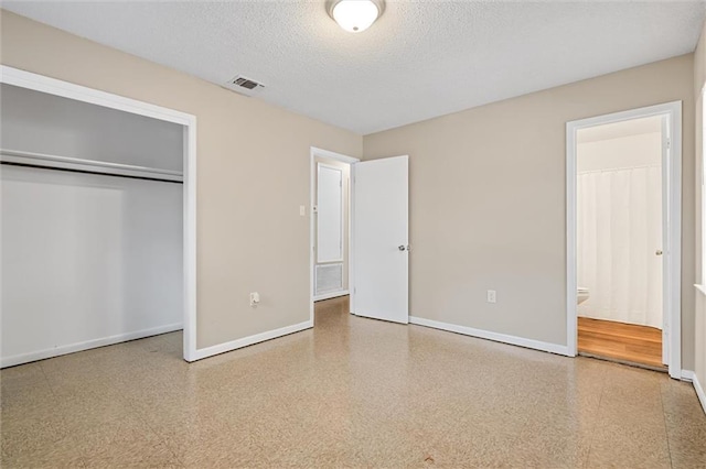 unfurnished bedroom featuring ensuite bath, a closet, and a textured ceiling