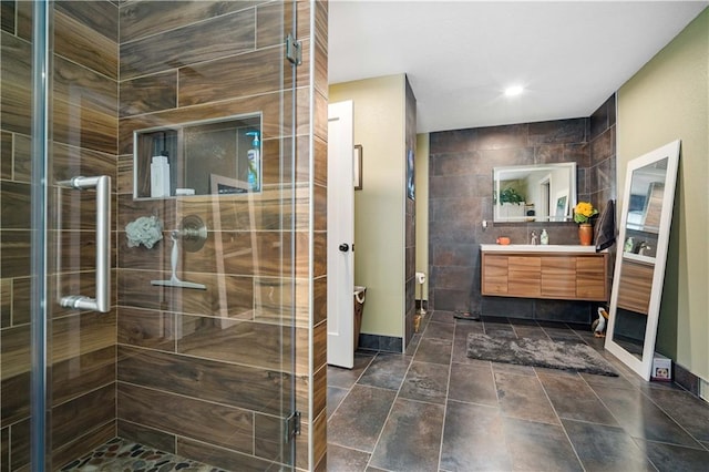 bathroom with tile walls, a shower with shower door, and vanity