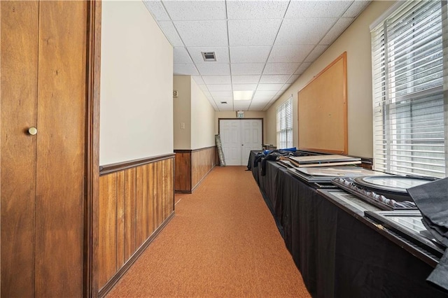 interior space featuring light carpet, a paneled ceiling, wood walls, and a wealth of natural light