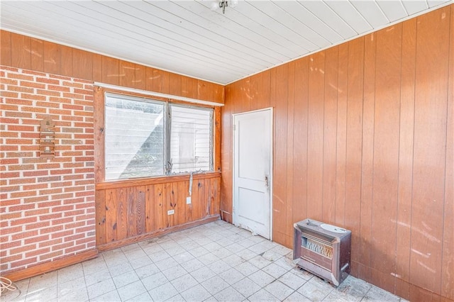 empty room with tile patterned floors, brick wall, wood walls, and a wood stove