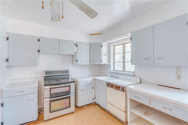 kitchen with dishwashing machine, light floors, open shelves, range with two ovens, and a sink