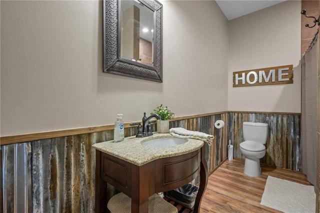 bathroom with a wainscoted wall, vanity, toilet, and wood finished floors