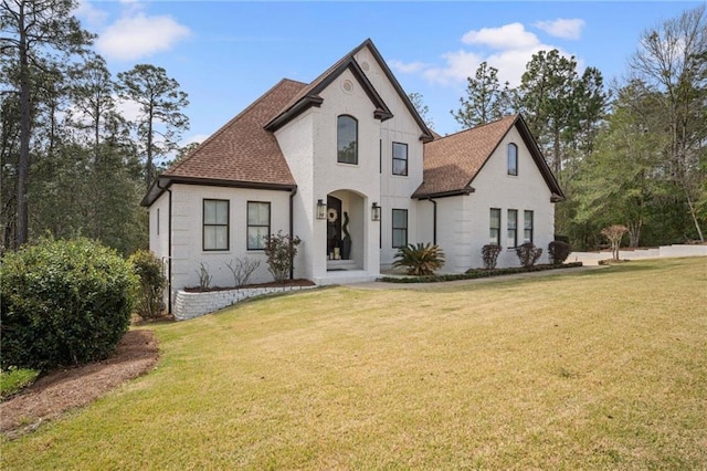 french provincial home with brick siding, roof with shingles, and a front yard