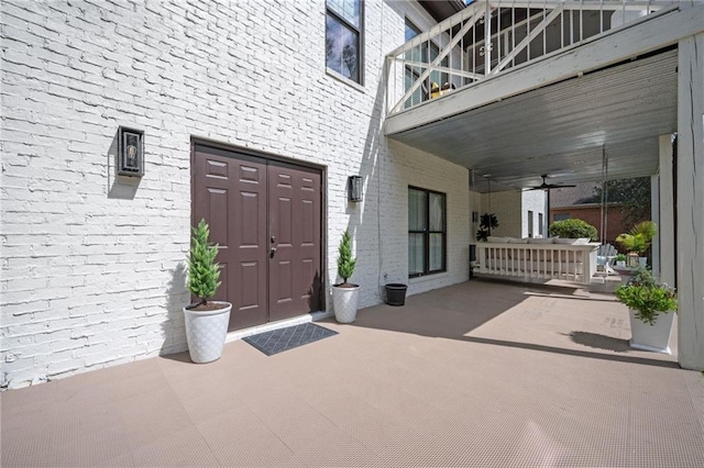 entrance to property featuring a balcony, a patio area, ceiling fan, and brick siding