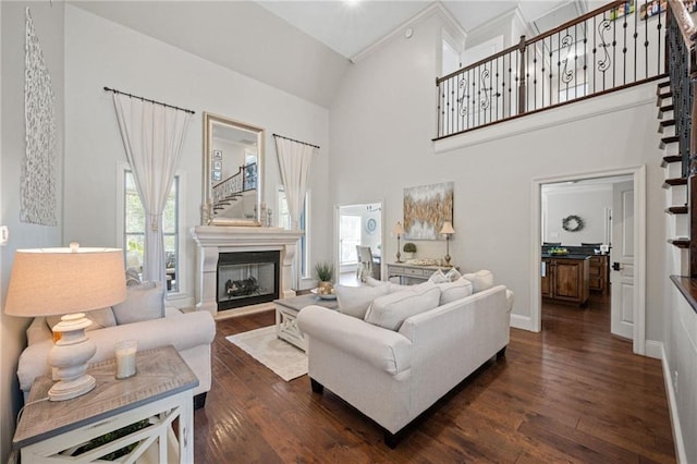 living area featuring baseboards, a fireplace with raised hearth, dark wood-style floors, stairs, and high vaulted ceiling