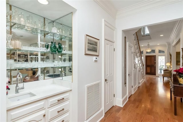 interior space with light wood finished floors, crown molding, visible vents, and a sink