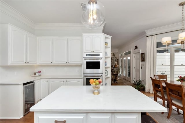 kitchen with stainless steel double oven, white cabinetry, hanging light fixtures, and beverage cooler