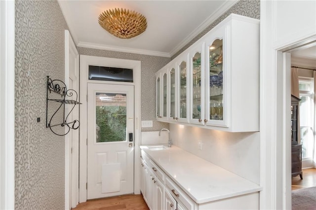 interior space featuring wallpapered walls, ornamental molding, light wood finished floors, and a sink