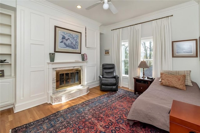 bedroom featuring recessed lighting, a premium fireplace, ornamental molding, a ceiling fan, and wood finished floors