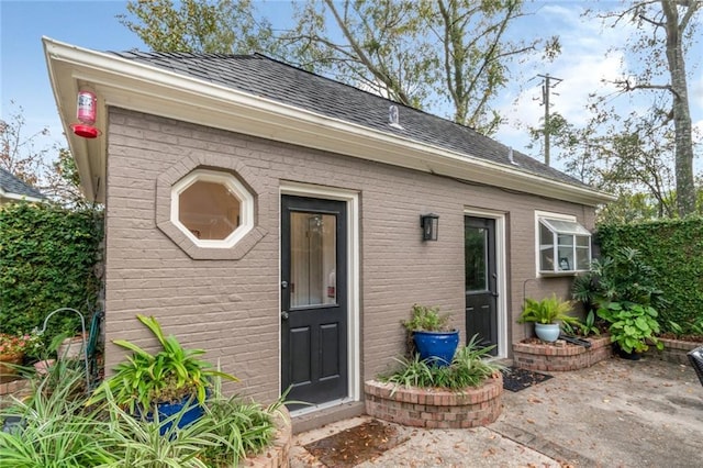 entrance to property featuring a patio, brick siding, and a shingled roof