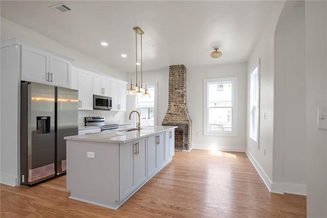 kitchen with light countertops, light wood finished floors, a center island with sink, appliances with stainless steel finishes, and a sink