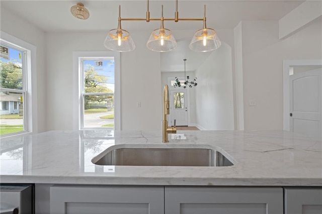 kitchen with a sink, decorative light fixtures, and light stone countertops