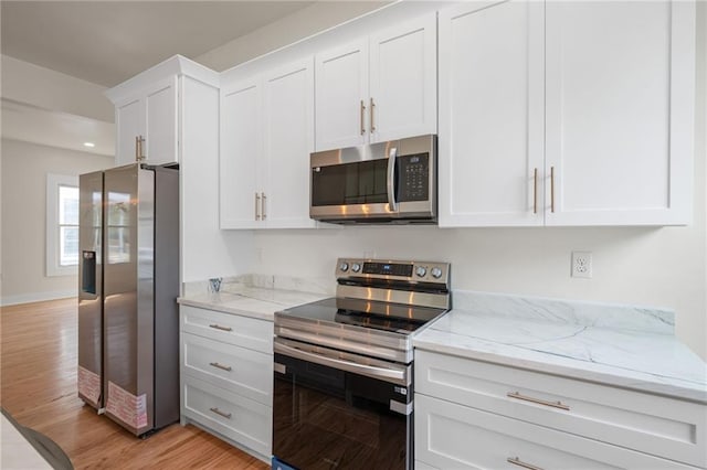 kitchen with white cabinets, light wood-style flooring, stainless steel appliances, and light stone countertops