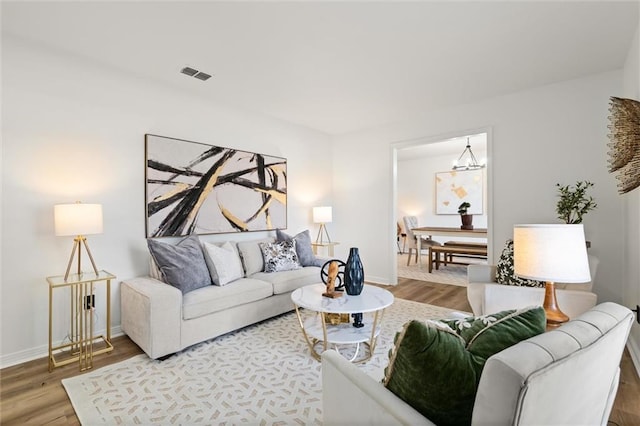 living room featuring an inviting chandelier, visible vents, baseboards, and wood finished floors