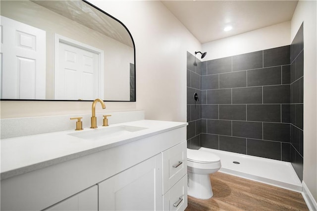 full bath with vanity, toilet, wood finished floors, and a tile shower