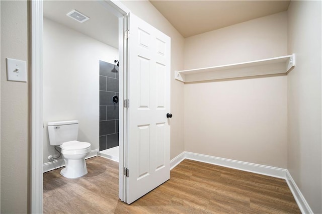 full bath featuring wood finished floors, visible vents, baseboards, a tile shower, and toilet