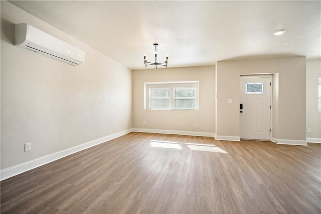 entrance foyer featuring baseboards, an AC wall unit, wood finished floors, and an inviting chandelier