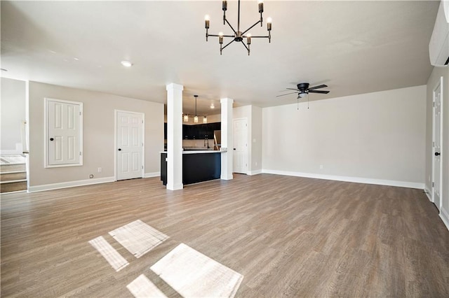 unfurnished living room with baseboards, light wood-style floors, a wall mounted AC, and ceiling fan with notable chandelier