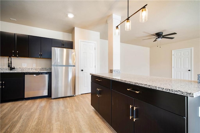 kitchen featuring light stone counters, light wood-style floors, appliances with stainless steel finishes, and dark cabinets