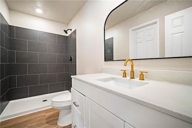 bathroom with vanity, toilet, wood finished floors, and a tile shower